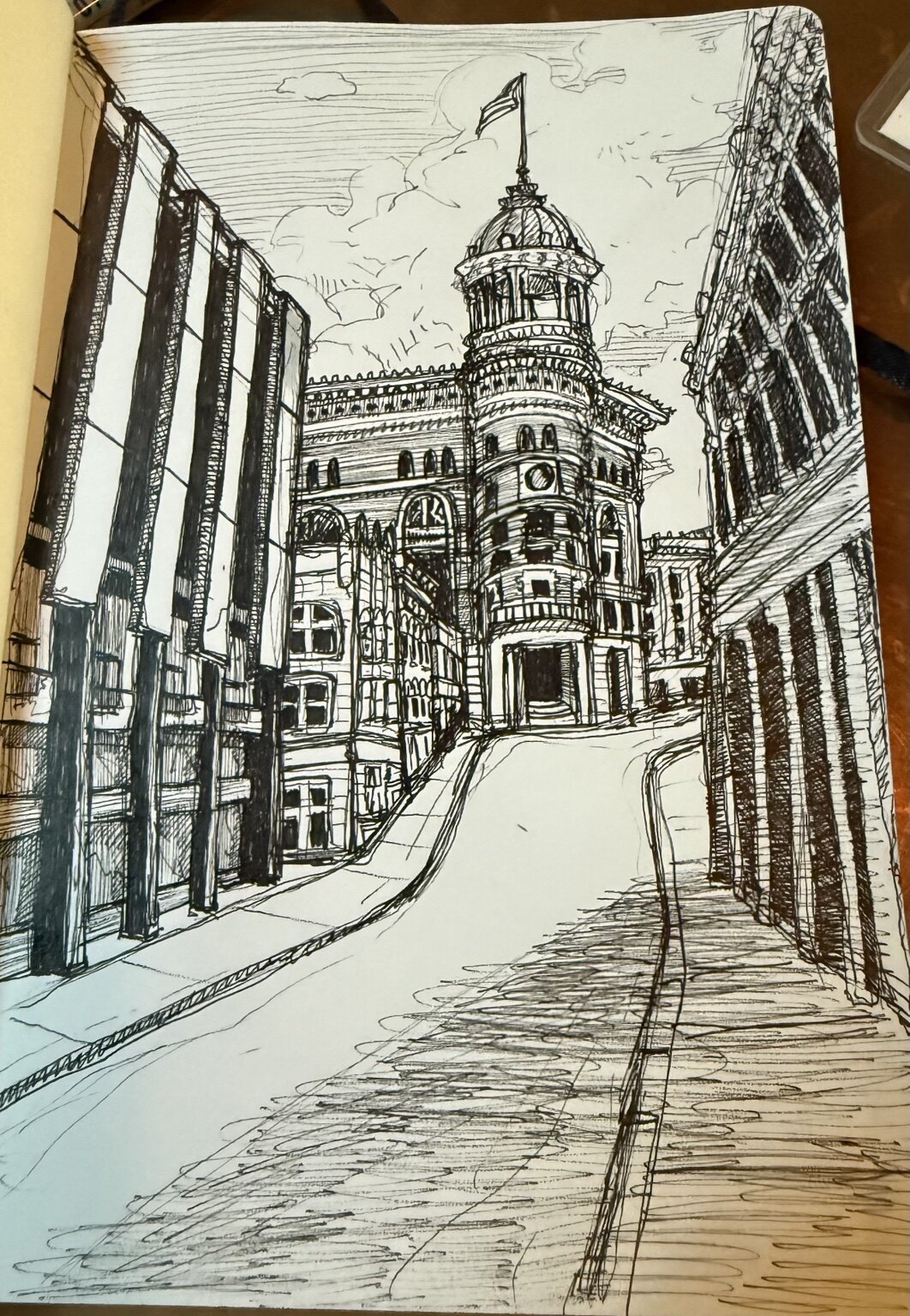 Black-and-white ink drawing looking uphill toward an ornate historic building between city structures.