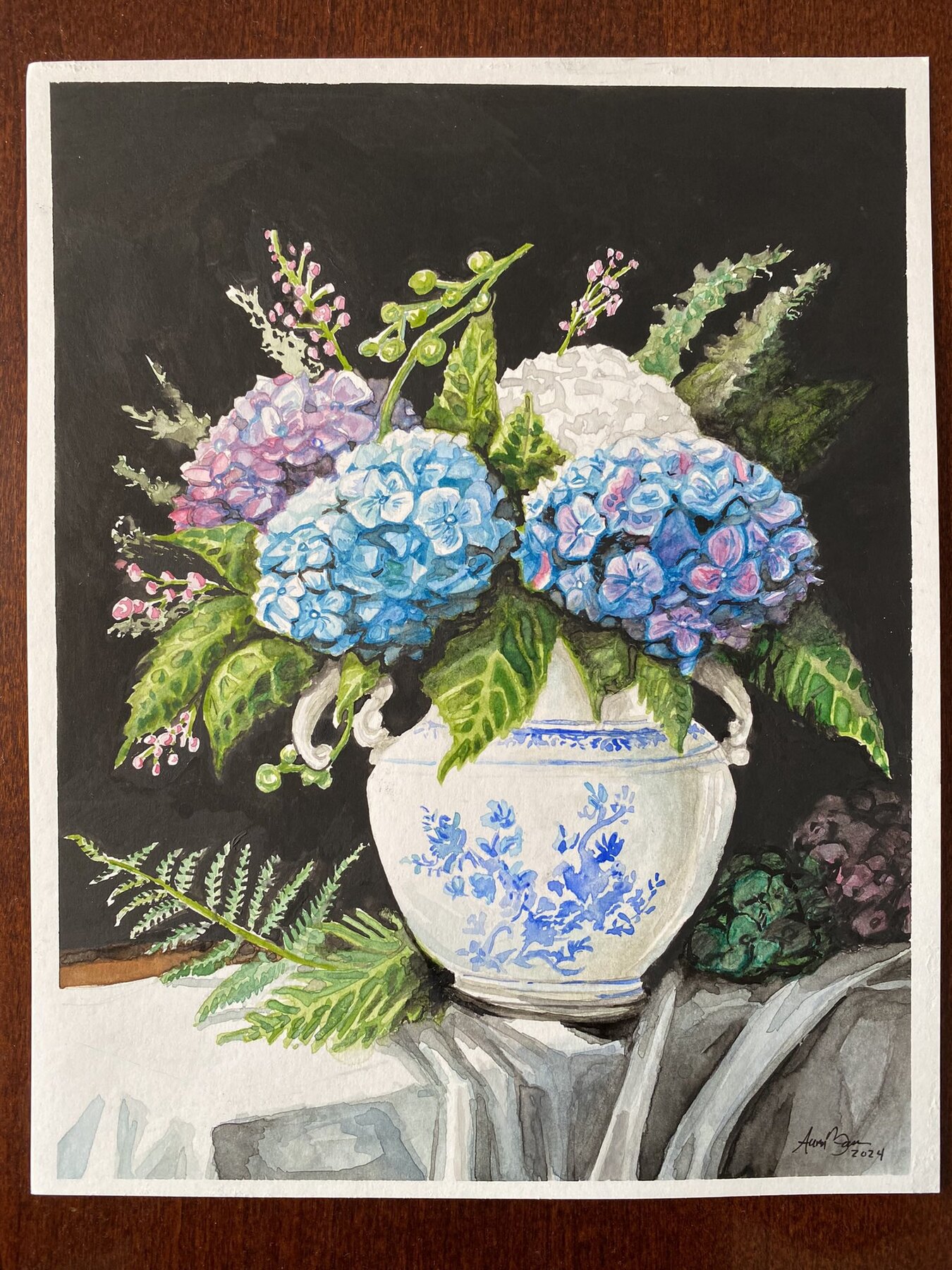 Watercolor painting of blue, white, and violet hydrangeas arranged in a blue-and-white vase against a black background.